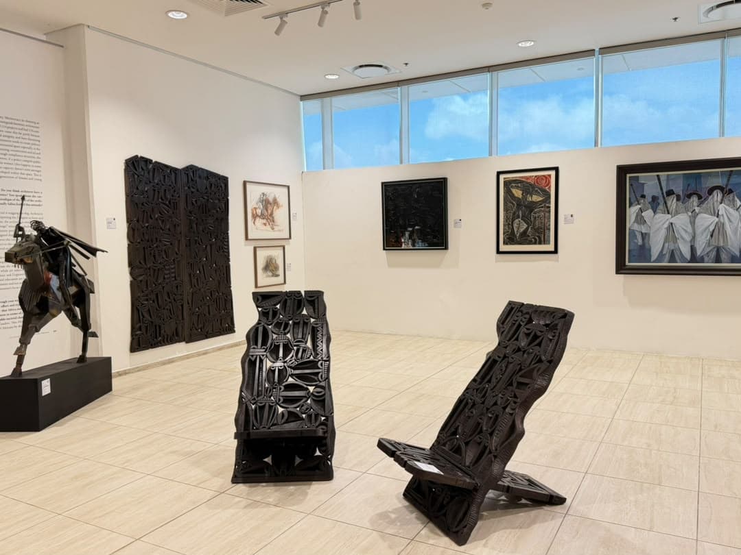 The carved chairs and the standing relief doors in the main room, with the wider programme on the walls behind.